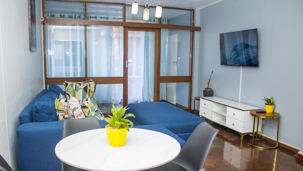 En moderne stue med en blå sofa, et rundt hvidt bord og et fjernsyn monteret på væggen.