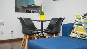 En moderne stue med en blå sofa, et rundt bord med to sorte stole, en guldfarvet potteplante og en farverig pude.