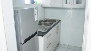 Une cuisine de taille réduite avec des meubles blancs, un évier en acier inoxydable et un réfrigérateur.