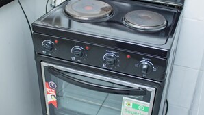 Une cuisinière noire, dotée de deux brûleurs et d’un four, est fixée à un mur blanc près d’une prise de courant.