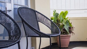 Zwei schwarze Korbstühle und ein Blumentopf auf einem Balkon.