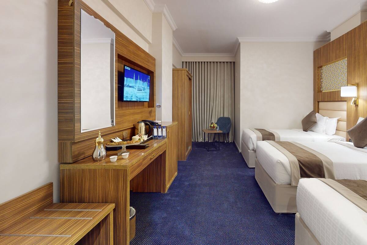 A hotel room with a large bed, a smaller bed, a desk with a TV, and a seating area with a chair and table.