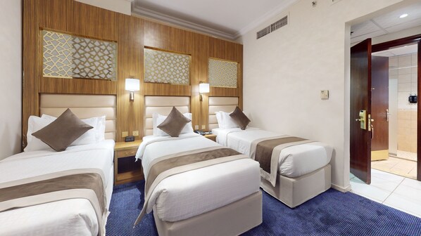 A hotel room with two single beds, a wooden headboard, a nightstand with a lamp, and a bathroom door. - Alansar platinum hotel (Madinah)
