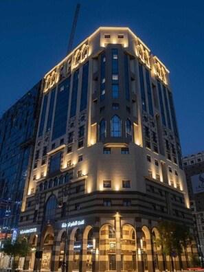 A multi-story hotel with a prominent arched entrance and illuminated signage. - Alansar platinum hotel (Madinah)