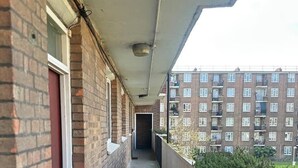 A narrow balcony with brick walls, a door, and a view of a multi-story building in the background. - Spacious Flat in Nine Elms (London)