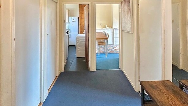 A hallway with a carpeted floor, white walls, and a ceiling fan. There are doors on both sides and a wooden bench in the foreground. - Spacious Flat in Nine Elms (London)
