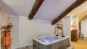 Una habitación con bañera de hidromasaje, una viga de techo de madera, un jarrón con flores secas y una lámpara.