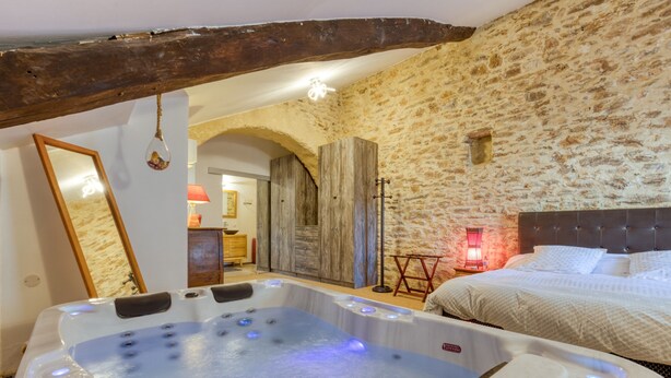 Una habitación con pared de piedra, viga de techo de madera, cama, bañera de hidromasaje y espejo.