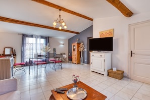 A living room with a wooden ceiling, a dining area with red chairs, a TV, and a fireplace. - Guest Room “La Forgerole” with Private Jacuzzi and Sauna (Faugères)
