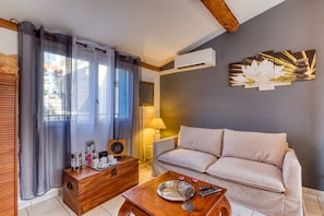 A room with a sofa, a wooden coffee table, a side table, a lamp, and a wall-mounted air conditioner. - Guest Room “La Forgerole” with Private Jacuzzi and Sauna (Faugères)