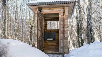 A wooden outdoor toilet structure in a snowy forest.