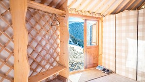 Un intérieur en bois avec un mur en treillis, une porte en bois donnant sur l’extérieur et une paire de chaussures posées sur le sol.