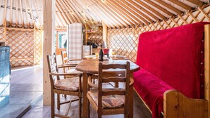 Une yourte avec un intérieur en bois, une table ronde, des chaises et un canapé recouvert d’une couverture rouge.