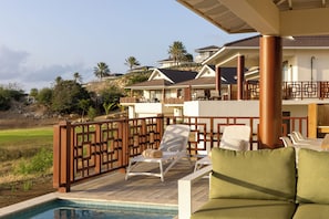 Zona de piscina con sillones de descanso, una terraza de madera y vistas a un campo de golf y edificios residenciales.