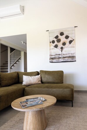 A living room with a sofa, a round coffee table with magazines, a wall-mounted artwork, and a staircase in the background. - Villa Jazmyn 6 Blue Bay Resort, pool, beach @300m, front row Golf Course (Willemstad)