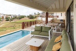 Un área junto a la piscina con un sofá blanco, una mesa y una parrilla.