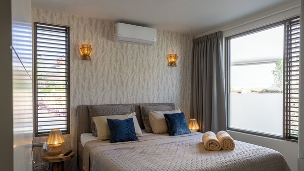 Une chambre d’hôtel avec un lit, deux lampes fixées au mur, un climatiseur et une fenêtre avec des rideaux.