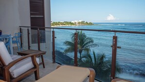 Un balcon avec deux fauteuils, une petite table et une vue sur l’océan et la plage.