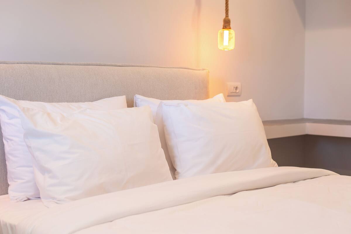 Un lit bien fait, avec du linge de lit blanc et des oreillers, une tête de lit et un luminaire suspendu.