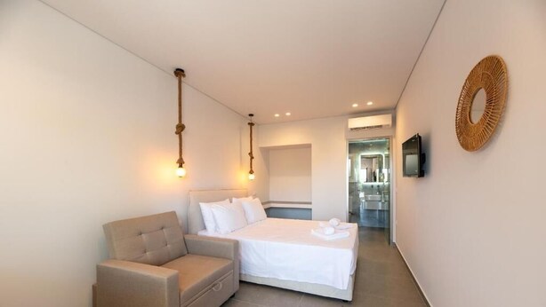 A hotel room with a bed, a sofa, a TV, and a wall-mounted decorative item. - AMELI COZY APARTMENTS  (Spata-Artemida)