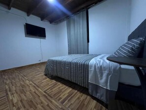 A room with a bed, a small table, a TV mounted on the wall, and a wooden floor. - Rustic Getaway in San Bartolo: Barbecue & Beach (San Bartolo)