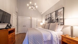 Een slaapkamer met een groot bed, een kroonluchter, een televisie en kunst aan de muur.