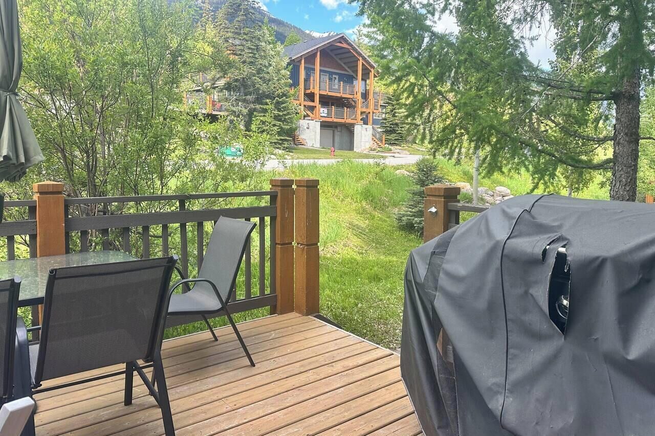 A wooden deck with a table and chairs, overlooking a cabin with a balcony.