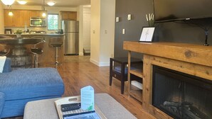 A modern kitchen with stainless steel appliances, a dining area with a wooden table and chairs, and a fireplace. - Aspens Retreat - 1BR w/Hot Tub (Golden)
