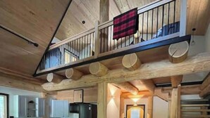 Un intérieur de cabine spacieux, avec un plancher en bois, un coin repas, une cuisine et un escalier menant à une mezzanine.