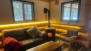 L’intérieur chaleureux d’un chalet avec un canapé, un fauteuil et un poêle à bois.