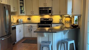 Een moderne keuken met witte kastjes, roestvrijstalen apparatuur, een centraal eiland met krukken en een kroonluchter.