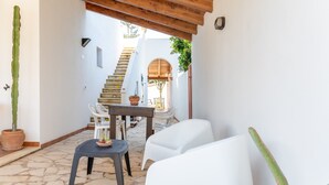 Eine Terrasse mit Steinboden, weißen Kunststoffstühlen, einem Tisch und Blumentöpfen.