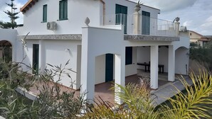 Ein zweistöckiges weißes Gebäude mit grünen Fensterläden, einem Balkon und einem Ziegeldach.