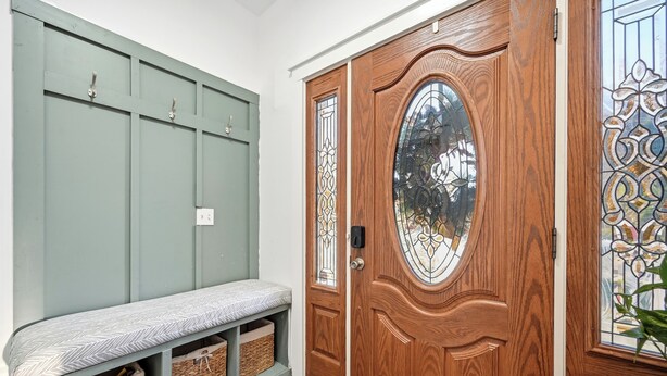 Une porte d’entrée en bois avec un panneau de verre, un banc doté de paniers de rangement et un mur végétal agrémenté d’un panneau perforé.