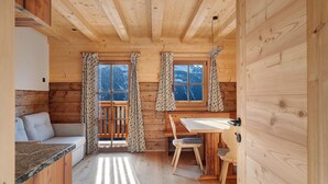 Interior de una cabaña de madera con sofá, mesa de comedor, sillas y cortinas.