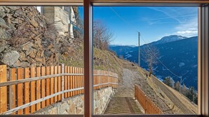 Vista a través de una ventana de una escalera de madera que desciende por una ladera rocosa, con una montaña al fondo.