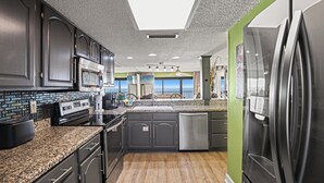 A modern kitchen with dark cabinetry, granite countertops, stainless steel appliances, and a view of the ocean.