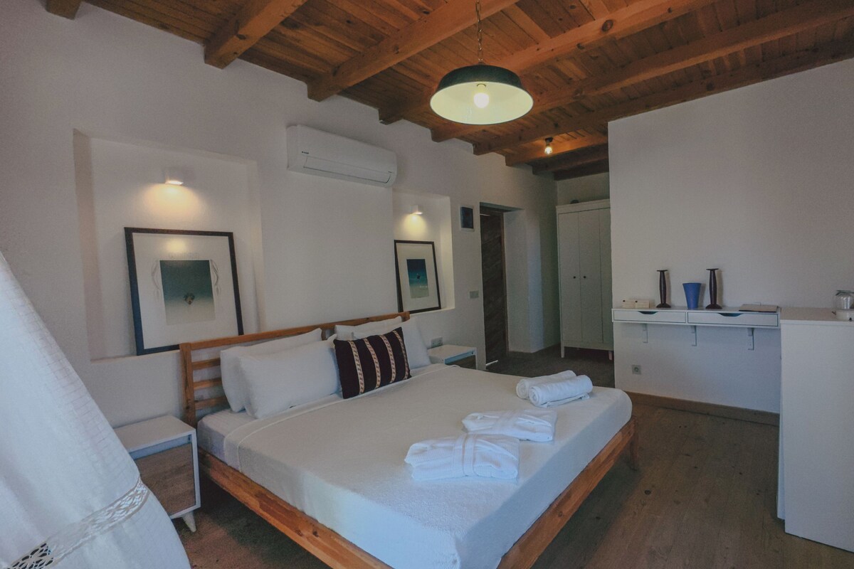 A bedroom with a wooden bed, white linens, a desk with a kettle, and a wardrobe.