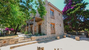 A stone building with a wooden balcony, surrounded by trees and purple flowers. - Gulhiz (Datca)