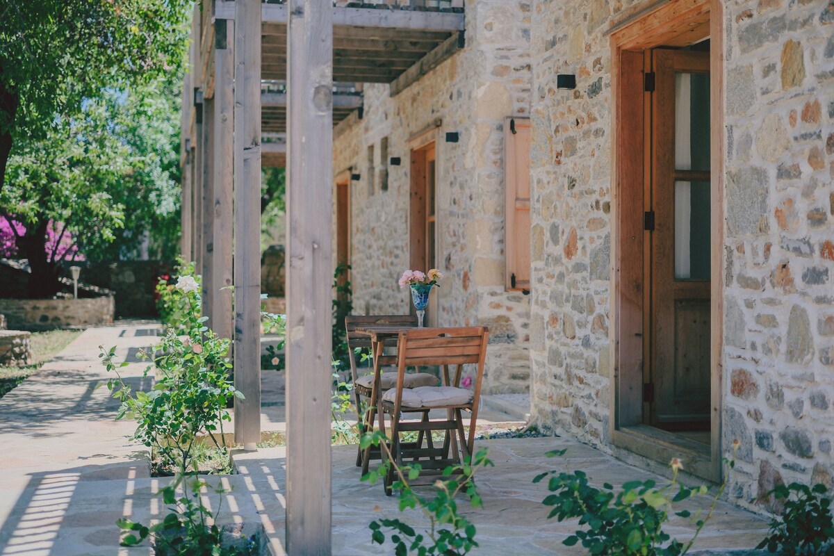 Un edificio de piedra con una mesa y sillas de madera, una puerta y un pequeño jardín.