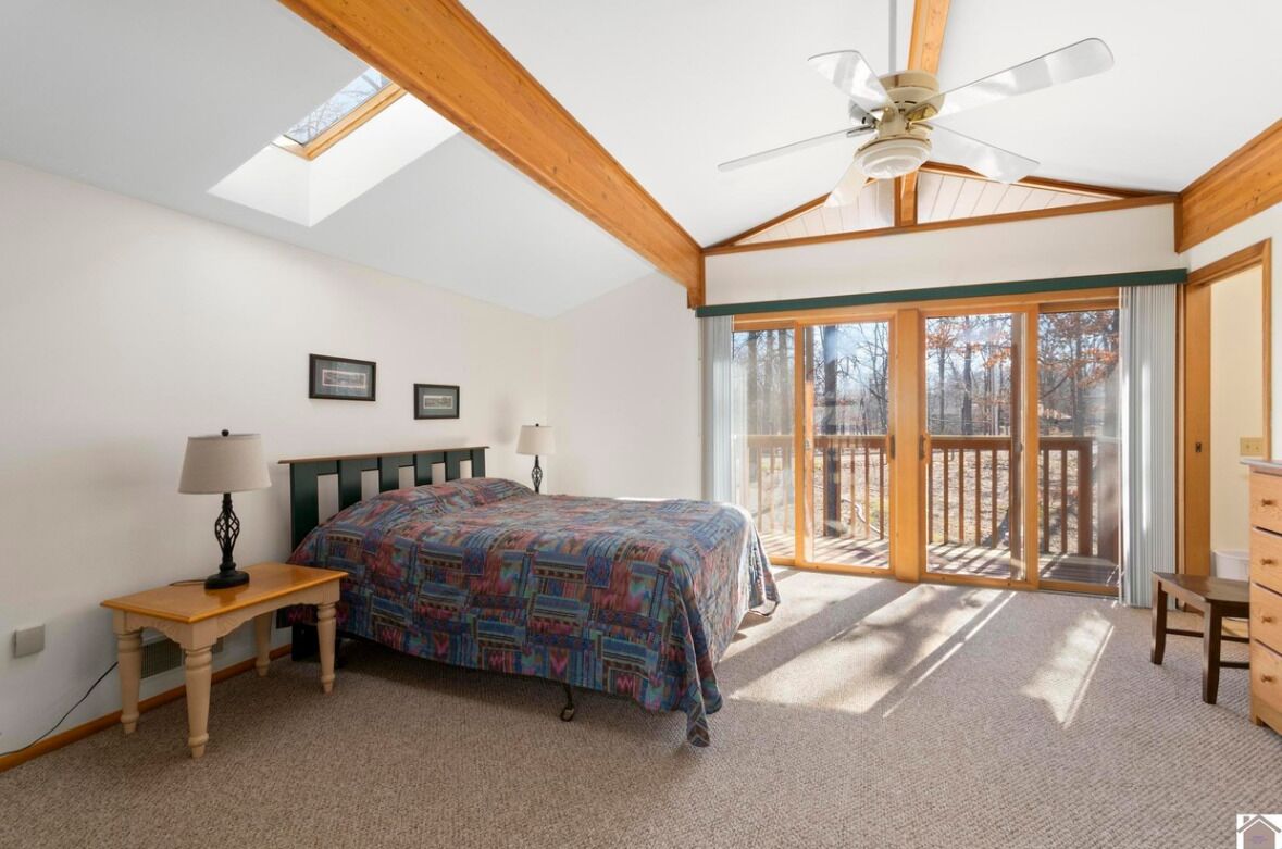 A bedroom with a bed, a nightstand, a dresser, a ceiling fan, and a large sliding glass door leading to an outdoor deck.