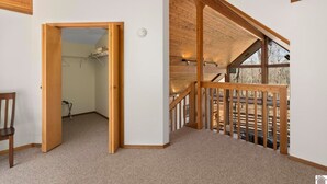 Una habitación amplia con techo alto, vigas de madera, un balcón con barandilla y una puerta que da a otra habitación.