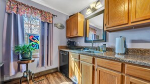 A kitchen with wooden cabinets, a granite countertop, a dishwasher, and a window with a colorful curtain.