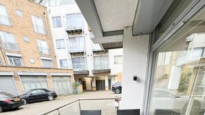 Ein Balkon mit Korbmöbeln, einem kleinen Tisch und Blick auf einen Parkplatz sowie Gebäude im Hintergrund.