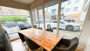 Ein moderner Essbereich mit Holztisch und schwarzen Stühlen, große Fenster mit Blick auf einen Parkplatz und Gebäude.