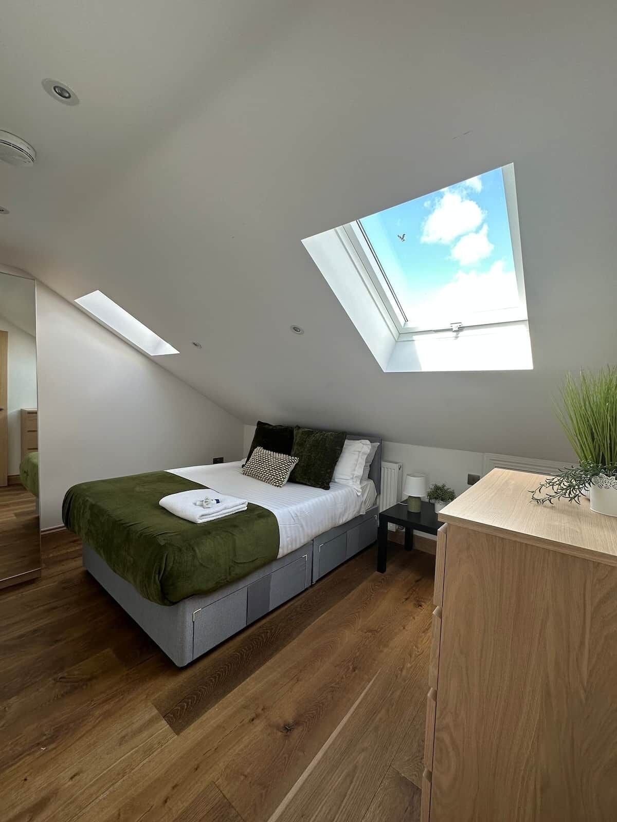 Ein modernes Schlafzimmer mit Oberlicht, einem Bett, einem Nachttisch und einer kleinen Pflanze.