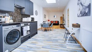 A modern kitchen with a washing machine, a dining area with a table and chairs, and a living room with a sofa. - Cornwall The Duchess 3 Bed Duplex 10 guests (London)
