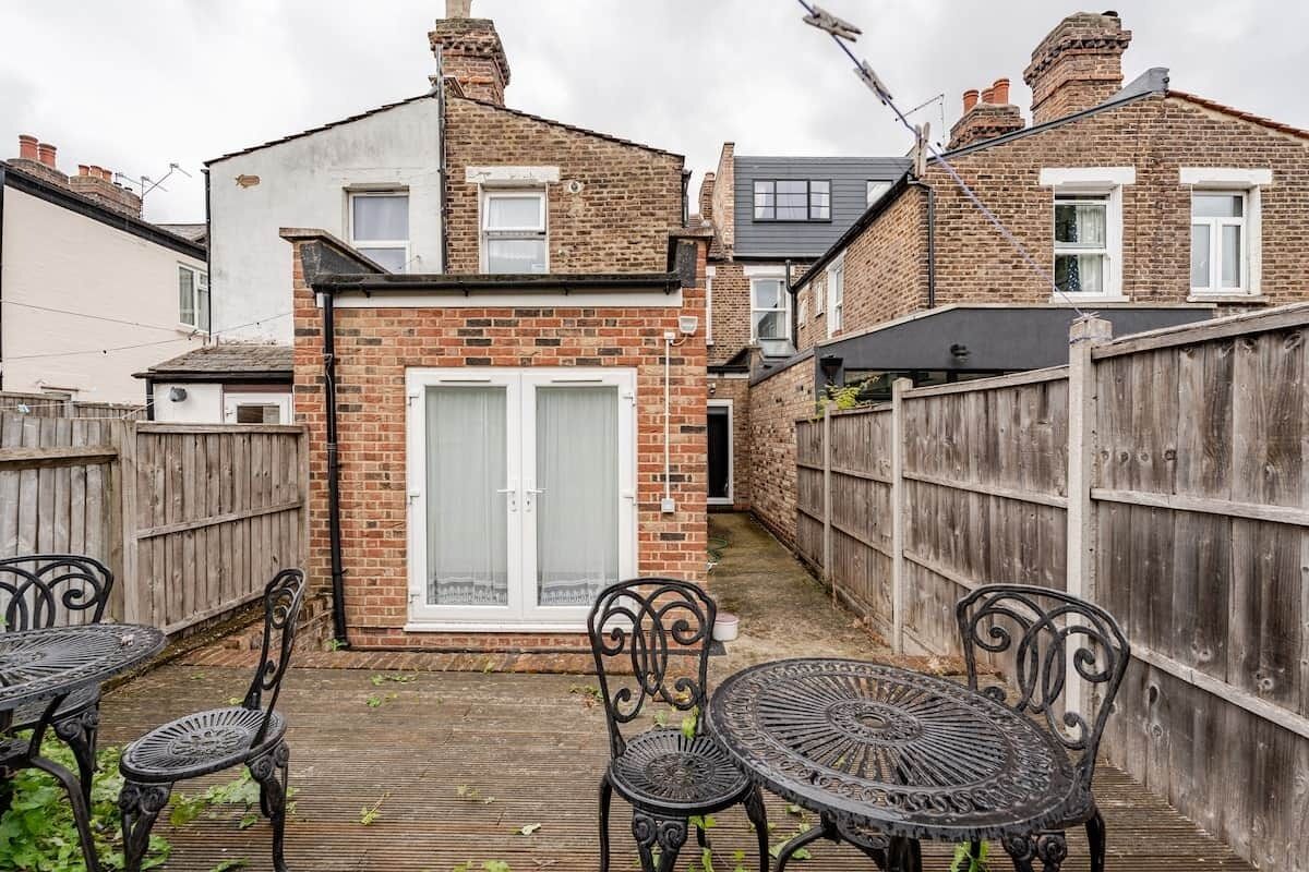 A narrow backyard with a brick house, a wooden fence, and metal outdoor furniture.