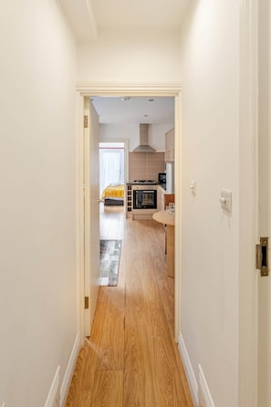 A hallway leading to a kitchen with a stove, oven, and cabinets. - Springfield - The Earl (London)