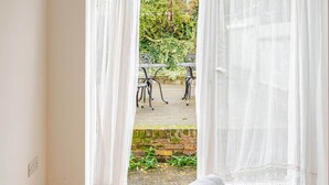 A bedroom with a bed, a yellow throw blanket, and a view of an outdoor patio with a table and chairs. - Springfield - The Earl (London)